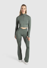 Grøn træningssæt bestående af en cropped jakke med høj krave og fuld lynlås, parret med højtaljede, flagrende leggings. Glat tekstur.