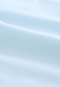 Hellblauer Stoff mit subtiler Gewebestruktur und sanften Falten, die zarte Schatten auf seiner Oberfläche erzeugen.