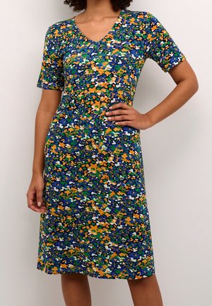 Femme portant une robe mi-longue à manches courtes avec un motif floral abstrait coloré en bleu, vert, orange, blanc et noir.