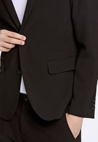 Zwart colbert van gladde stof, met een notch-revers, twee voorzakken en vijf zwarte knopen op de mouw.