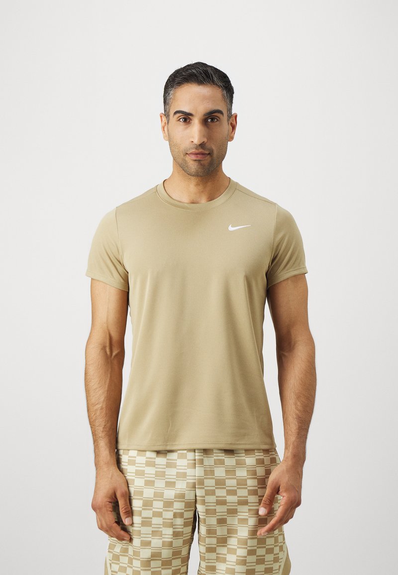 Beige kortermet treningsskjorte med rund hals og hvit Nike-logo på venstre bryst, kombinert med rutete beige shorts.