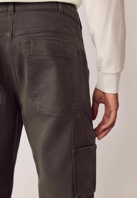 Dunkelgraue Cargo-Hosen mit schlanker Passform, Gesäßtaschen und einem strukturierten Stoff. Sichtbare Nähte und Seitentaschen verbessern die Funktionalität.