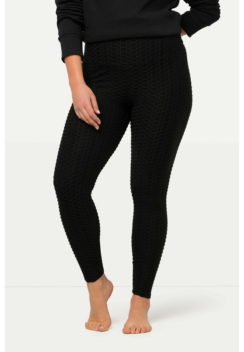 Leggings noirs avec un motif texturé présentant un design en cubes en relief, fabriqués dans un matériau extensible, épousant les hanches et les jambes.
