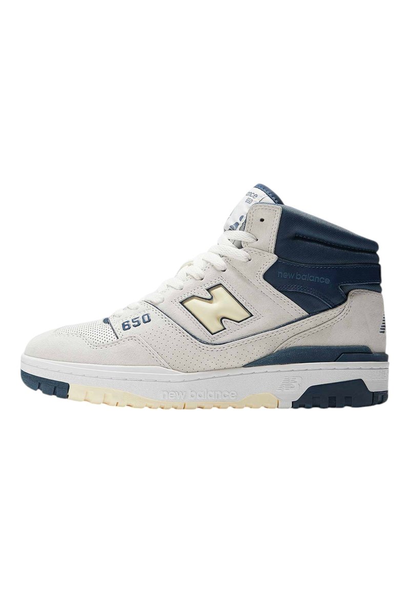 High-top sneaker in off-white suede with navy accents. Features perforated toe box, padded collar, and thick rubber sole with contrasting tread.