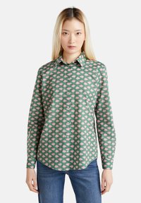Camicia verde con bottoni, con un motivo floreale rosa, maniche lunghe e colletto a punta. Il tessuto appare liscio, con una vestibilità comoda.