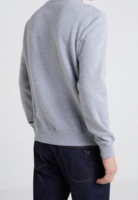 Felpa grigia realizzata in tessuto morbido, con maniche lunghe, polsini a coste e fascia in vita. La vista posteriore mostra un design semplice senza motivi.