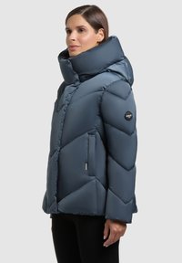 Tume sinine talvejope kõrge kraega, siksakmustriga, tõmbluku ja küljetaskutega, valmistatud siledast, läikivast materjalist.