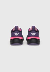 Lilla og rosa treningssko med teksturert overdel, avrundet hæl og en svart gummisåle med logo akcent på baksiden.