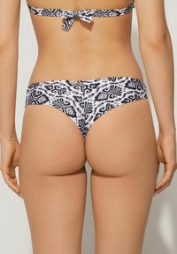 Parte inferior de bikini de estampado en blanco y negro con corte bajo y banda ancha. Hecha de tejido suave, con un clásico lazo en la parte trasera.