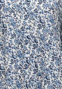 Tissu blanc avec imprimé floral bleu et noir, comprenant de petites fleurs, des feuilles, et des boutons blancs au centre.