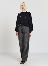 Schwarzer Sweatshirt mit silbernen Punktakzenten, kombiniert mit hoch taillierten, weit geschnittenen grauen Jeans. Modell trägt dunkle Schuhe. Schlichter Hintergrund.