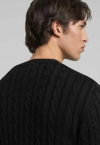 Pull noir en maille avec un motif torsadé, doté d'un col rond côtelé et d'une finition texturée. Vue de dos, montrant le détail des épaules.