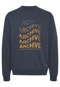 Sudadera navy con "ARCHIVE" impreso repetidamente en un degradado de amarillo a negro y la frase "Algo fuerte, estable y confiable. Apunta a algo sólido."