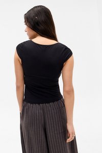 Woman with long dark hair wearing a fitted black short-sleeve top and high-waisted gray pinstripe pants, facing away against a white background.