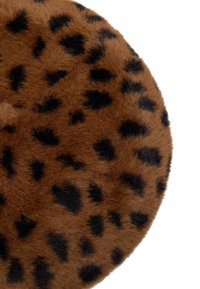 Okrągła, brązowa poduszka z futerka syntetycznego z czarnymi łatami w panterkę, charakteryzująca się miękką fakturą i gładkim, okrągłym kształtem. Brak widocznych elementów montażowych.
