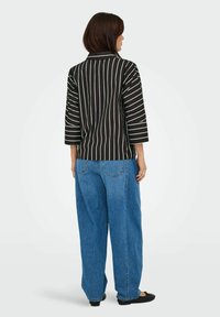 Zwart gestreept shirt met een kraag en driekwartmouwen, gecombineerd met een wijde spijkerbroek in het blauw, gezien vanuit de achterkant.