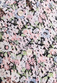 Gros plan d'une chemise boutonnée avec un motif floral dense comportant des fleurs blanches, roses, bleues et vertes sur un fond noir.