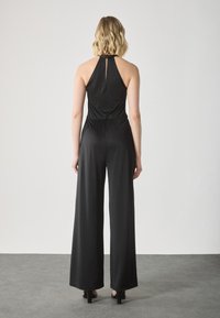Mono negro con cuello halter, diseño de pierna ancha y detalle de abertura en la espalda. Hecho de una tela suave con una cintura ajustada y un elegante caído.