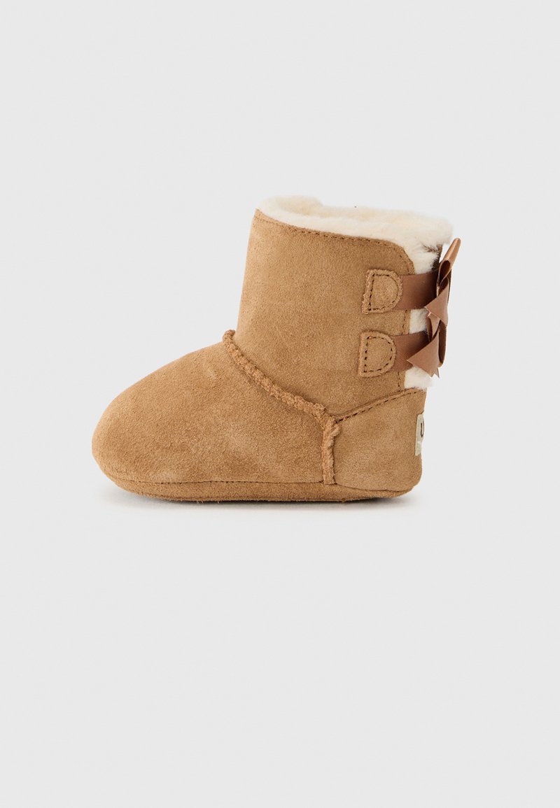 Botte en daim tan avec un revers doublé de fourrure crème, présentant deux sangles marron avec des nœuds sur le côté et des détails de couture.