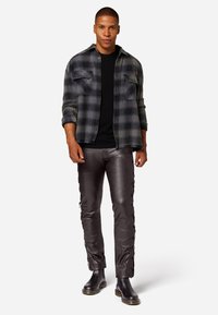 Flanellen overhemd in zwart en grijs ruitpatroon, zwart t-shirt, strakke grijze leren broek met veters, zwarte enkellaarsjes.