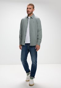 Ljusgrön skjorta med lång ärm, kombinerad med en vit t-shirt och blå jeans. Skorna är vita med gröna accenter.