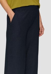 Marineblauwe wijde broek met ribbelstructuur, voorzien van zijzakken en een elastische tailleband. De stof lijkt zacht en lichtgewicht.