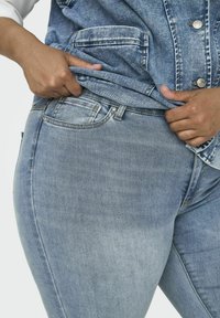 Jeans de denim azul claro con una textura suave, que presentan un diseño clásico de cinco bolsillos y una forma ajustada en la cintura y las caderas.