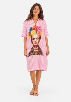 Femme portant une robe rayée rose et blanche avec un grand portrait coloré d'une femme avec des fleurs dans les cheveux à l'avant.