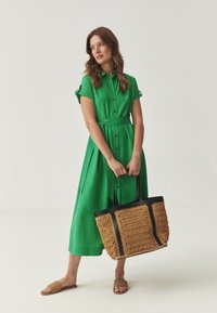 Zelené šaty na knoflíky s krátkými rukávy, páskované v pase. Woven béžová taška s černými akcenty, spárovaná s hnědými skládacími sandály.