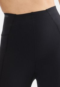 High-waisted black leggings made of stretchy fabric with flat seams and a pocket on the side for convenience.