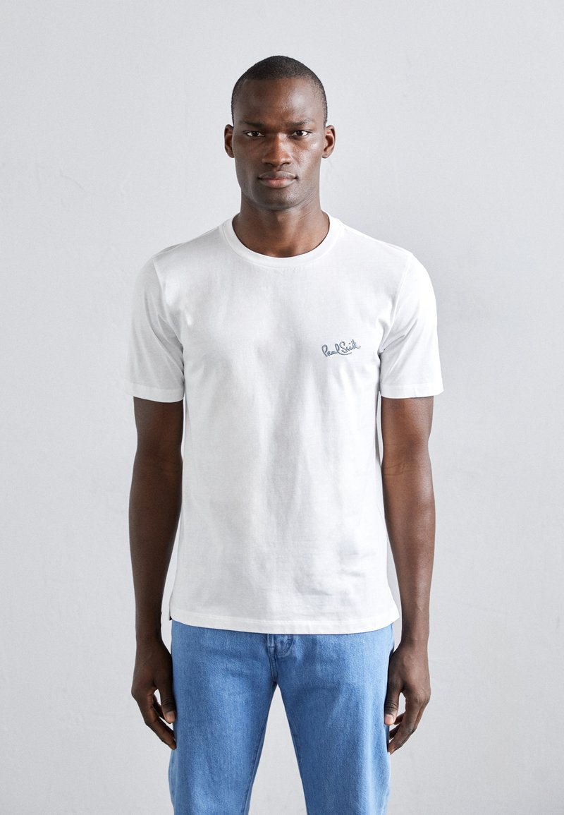 Valge puuvillane t-särk lühikeste varrukatega, ümar kaelus ja diskreetne sinine logo vasakul rinnal. Kombineeritud helesiniste teksadega.