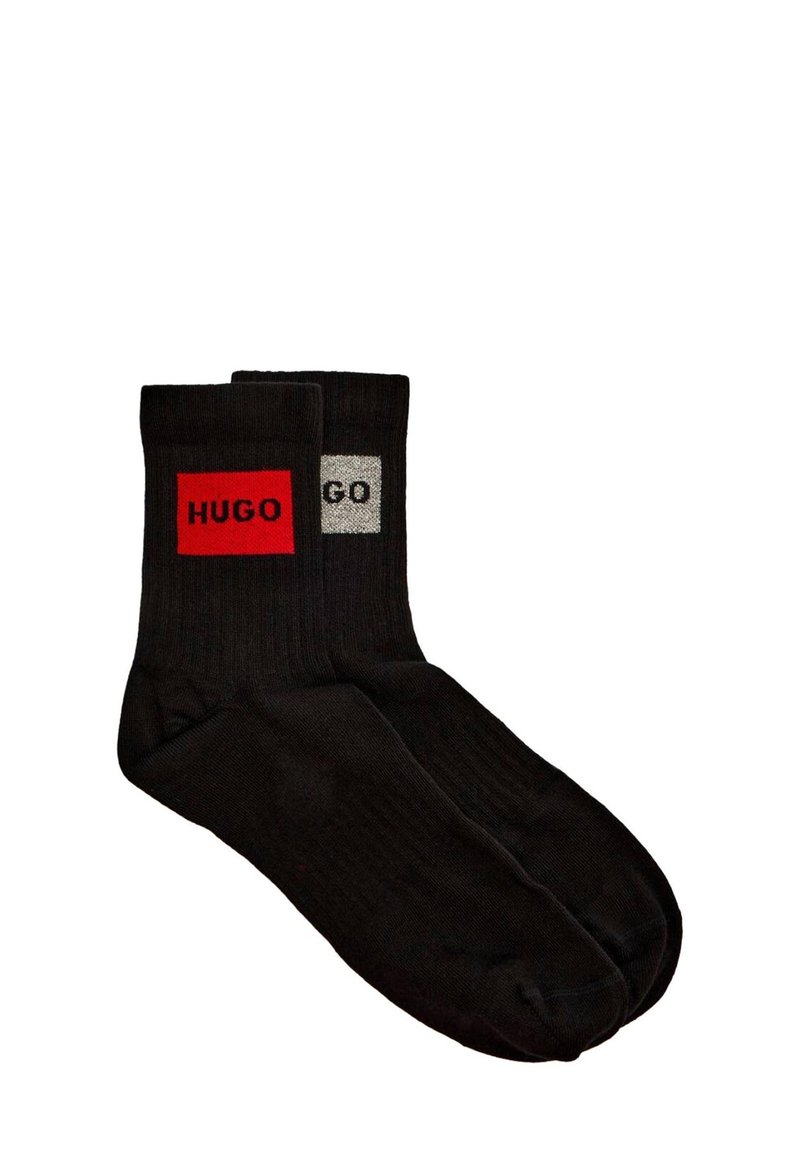 Calcetines negros de algodón con un parche rectangular rojo que lleva el texto "HUGO" en uno y un parche gris con el texto "GO" en el otro. Textura acanalada.