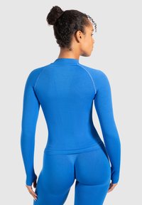 Langærmet activewear-top i livlig blå. Tætsiddende design, ribbet tekstur, flade sømme og høj hals. Bæres med matchende bukser.