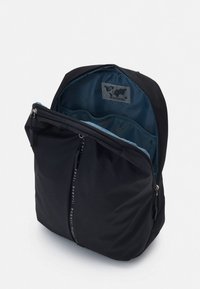 Μαύρο σακίδιο με λεία εξωτερική επιφάνεια, κεντρικό διαμέρισμα με φερμουάρ και μπλε εσωτερικό. Διαθέτει μπροστινή τσέπη και λογότυπα ως διακοσμητικά στοιχεία.