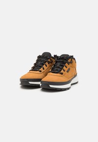 Brown suede hiking shoes with black laces, rubber soles, and white midsole. Features padded collar and textured accents on the upper.