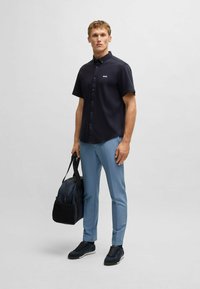 Short-sleeve navy shirt with a button-down collar, paired with light blue pants, and black sneakers. A dark bag is held in one hand.