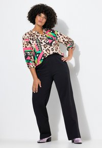 Kleurrijke top met panterprint, geometrische patronen in roze en groen, en zwarte accenten. Zwarte broek en glanzende lichtpaarse schoenen.