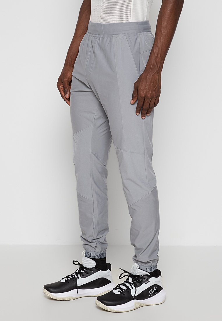 Pantalons de sport gris clair avec une coupe ajustée, taille élastique et panneaux contrastés. Portés avec des baskets noires et blanches.