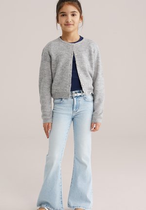 Pilkas megztas kardiganas su apvalia iškirpte, sagomis priekyje, ilgomis rankovėmis, derinamas su šviesiai mėlynais plačiais džinsais ir tamsiai mėlynu viršutiniu drabužiu.