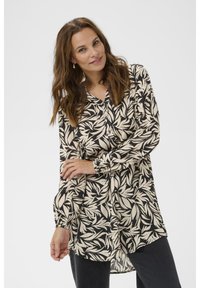 Blouse à manches longues en crème et noir avec imprimé feuilles, présentant un devant boutonné, une coupe décontractée et des poignets de manches froncés.