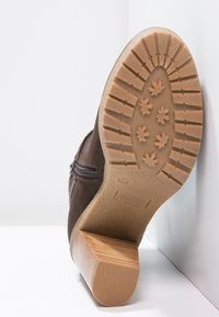 Brun mockaskinnsankleboot med dragkedja, med en strukturerad gummisula och klack med blockdesign. Stjärnmönstrad sula för grepp och stabilitet.