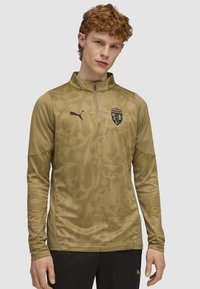 Langærmet pullover i olivengrøn med et tekstureret mønster. Har en kvart lynlås og et sort Puma-logo på brystet.