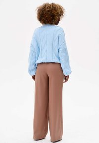 Lichtblauwe gebreide trui met een kabelbreipatroon, gecombineerd met high-waisted, wijde bruine broeken. De stoffen lijken zacht en comfortabel.
