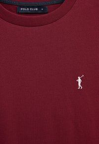 Maglietta bordeaux girocollo con piccola ricamo bianco del giocatore di polo sul petto e etichetta nera "POLO CLUB" all'interno del colletto, taglia media.