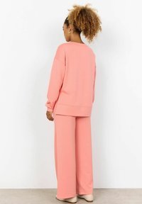 Maglione rosa con vestibilità comoda e pantaloni a gamba larga realizzati in un tessuto morbido, caratterizzati da polsini a costine e un design semplice senza decorazioni.