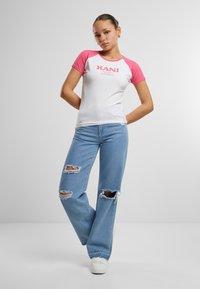 T-shirt à manches courtes blanche et rose avec le texte "KANI". Associé à un jean large délavé bleu clair et des baskets blanches.