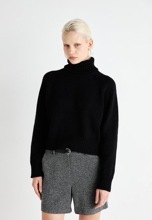 Svart strikket høyhalset genser med ribbestrikket kant og mansjetter, kombinert med grå strukturerte shorts med et svart belte. Enkel og moderne silhuett.