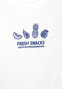 Bílá tkanina se modrou výšivkou různých druhů ovoce: plátek melounu, avokádo, ananas a dva neurčené kusy ovoce. Text zní "ČERSTVÉ SNACKY OBLAST JIŽNÍHO ZÁLIVU."