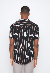 Chemise à manches courtes, colée, en tissu noir avec des motifs abstraits verticaux en blanc, beige et rouille ; coupe décontractée avec un ourlet arrondi.