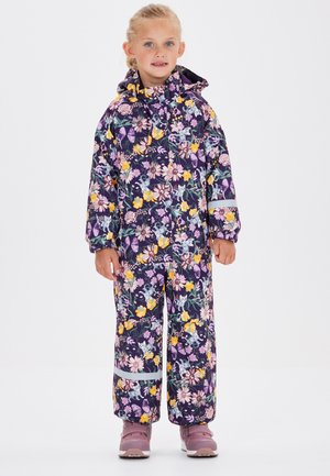 Combinaison de ski à motifs floraux avec un fond violet foncé et des accents jaunes, roses et verts. Comprend une capuche et des bandes réfléchissantes.